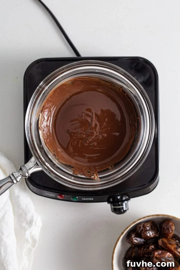Decadent Chocolate Peanut Butter Dates 7 A bowl of rich, dark melted chocolate sitting atop a homemade double boiler setup on a small cooktop, illustrating the melting process.