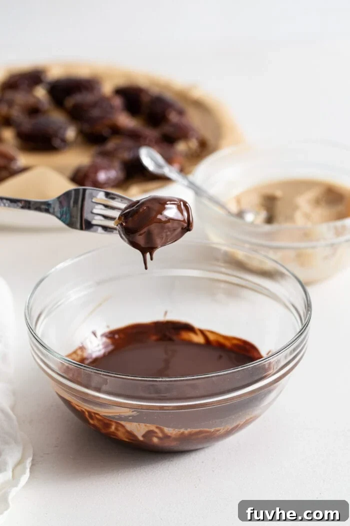Decadent Chocolate Peanut Butter Dates 8 A fork carefully lowering a mousse-stuffed date into a bowl of glossy melted chocolate, ensuring a complete and even coating.