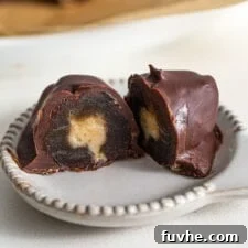 A perfectly halved chocolate-covered Medjool date with a creamy peanut butter filling on a small plate, ready to be enjoyed.
