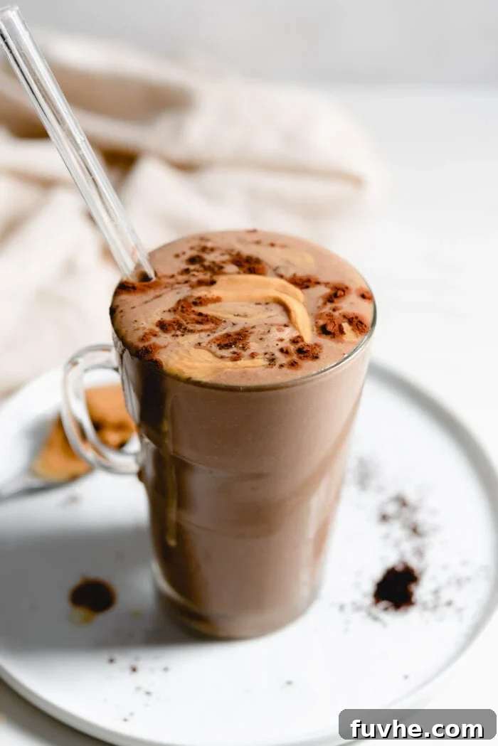 Creamy chocolate smoothie in a glass mug with a straw, hinting at rich coffee and peanut butter flavors.
