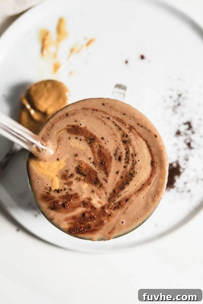Rich chocolate smoothie, possibly with cinnamon, in a clear glass, perfect for a coffee and peanut butter blend.