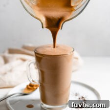 A blender pouring a thick, creamy chocolate smoothie into a glass mug, illustrating the delicious texture of the peanut butter coffee smoothie.