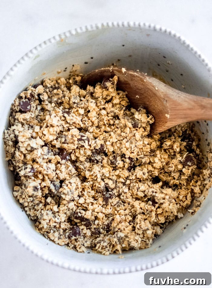 Chocolate chip oatmeal dough in a mixing bowl with a wooden spoon resting in bowl.
