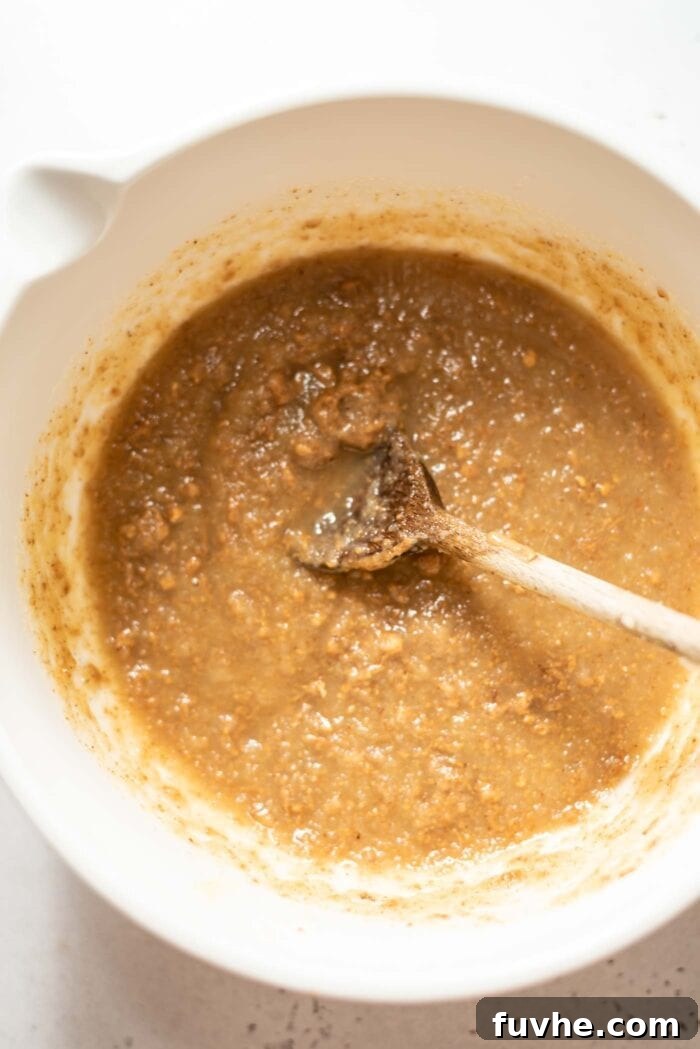 Plant-Powered Protein Muffins 4 Almond butter mixing with applesauce and maple syrup in a mixing bowl with a spoon, showing the smooth consistency of the wet ingredients.