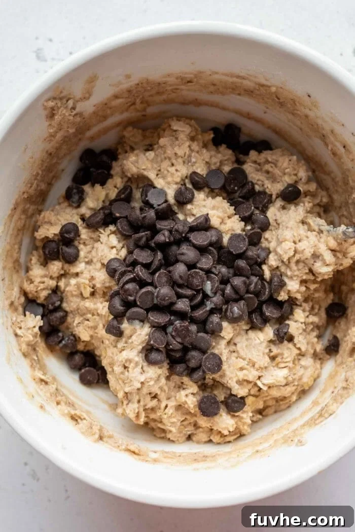 Plant-Powered Protein Muffins 6 Dairy-free chocolate chips being added to a mixing bowl of thick muffin batter, ready for folding.