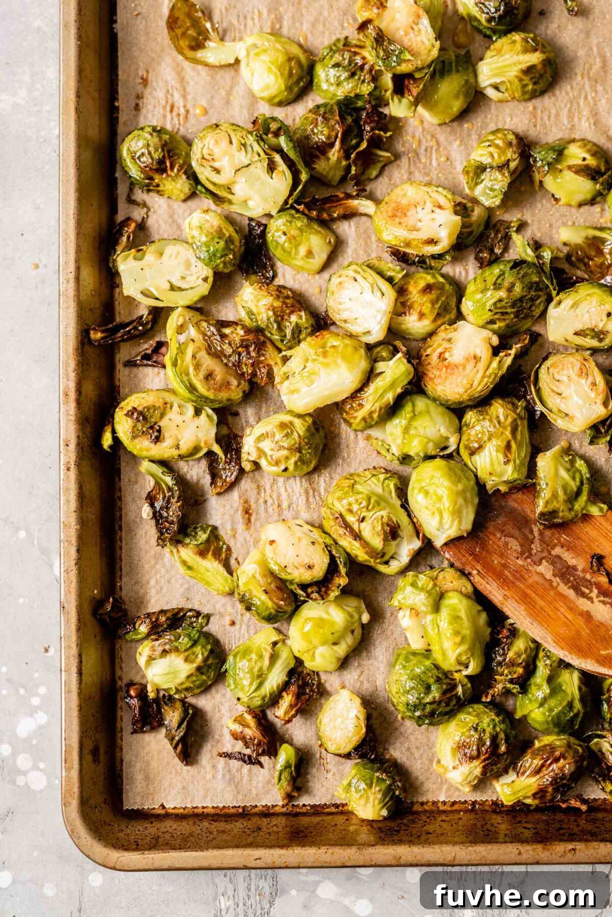 Caramelized Maple Dijon Brussels Sprouts 7 Roasted Brussels sprouts being tossed with maple dijon glaze on a baking tray with a wooden spatula.