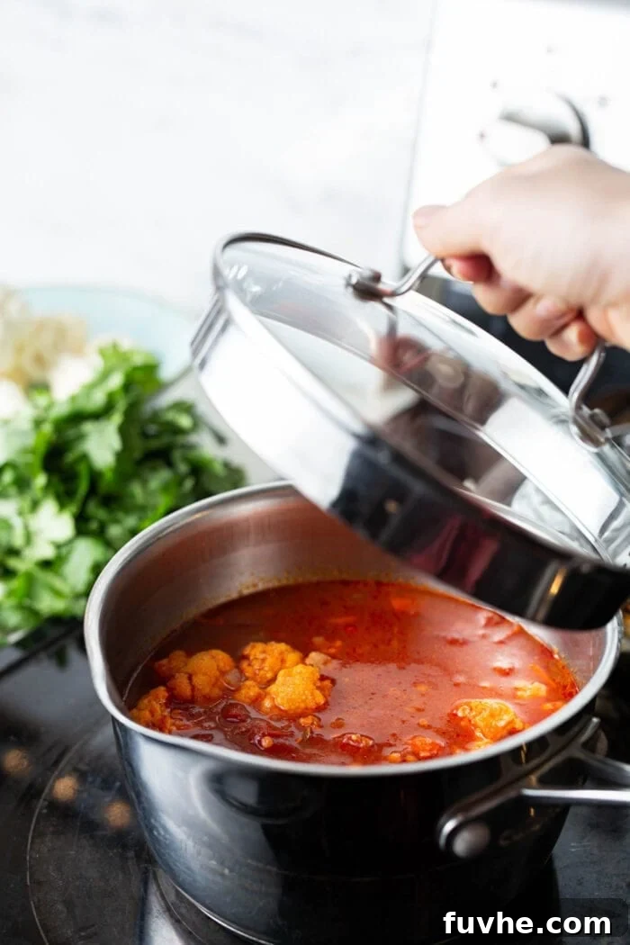 A pot of red lentil cauliflower curry stew, with the lid just placed on top, ready to simmer.