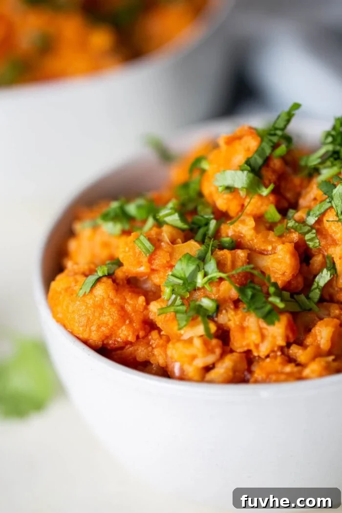 A close up of a white bowl of red lentil cauliflower curry beautifully topped with fresh cilantro, ready to eat.