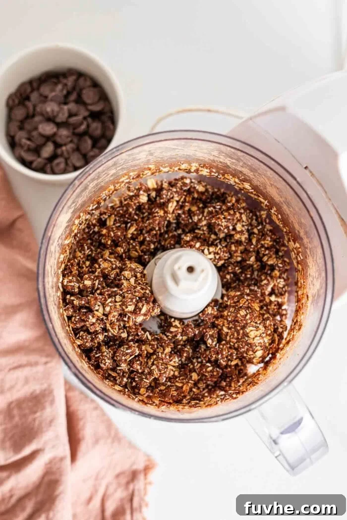 A chocolate oat and date dough blend in a food processor, ready to be pressed into a pan.