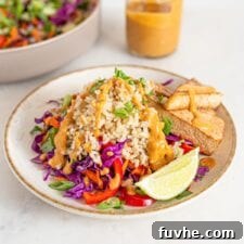 Bowl of colorful salad with brown rice, peanut sauce, tofu and veggies. Jar of sauce in background.