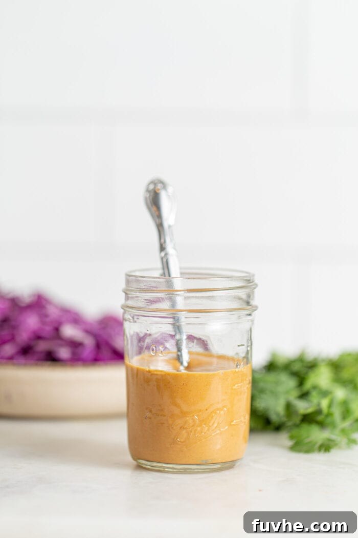 A glass jar filled with luscious, creamy peanut sauce, with a spoon resting invitingly in it, ready to be drizzled over the salad.