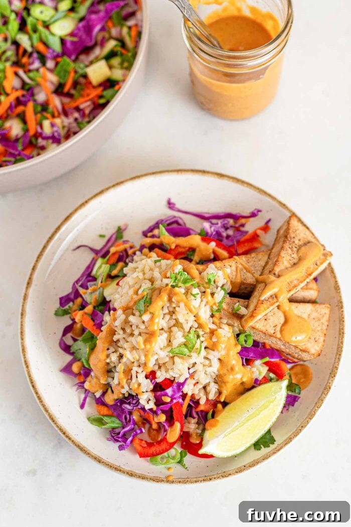 A beautifully plated serving of Thai chopped salad, showcasing the harmonious arrangement of brown rice, fresh, vibrant veggies, crispy baked tofu, and a rich peanut sauce drizzle.