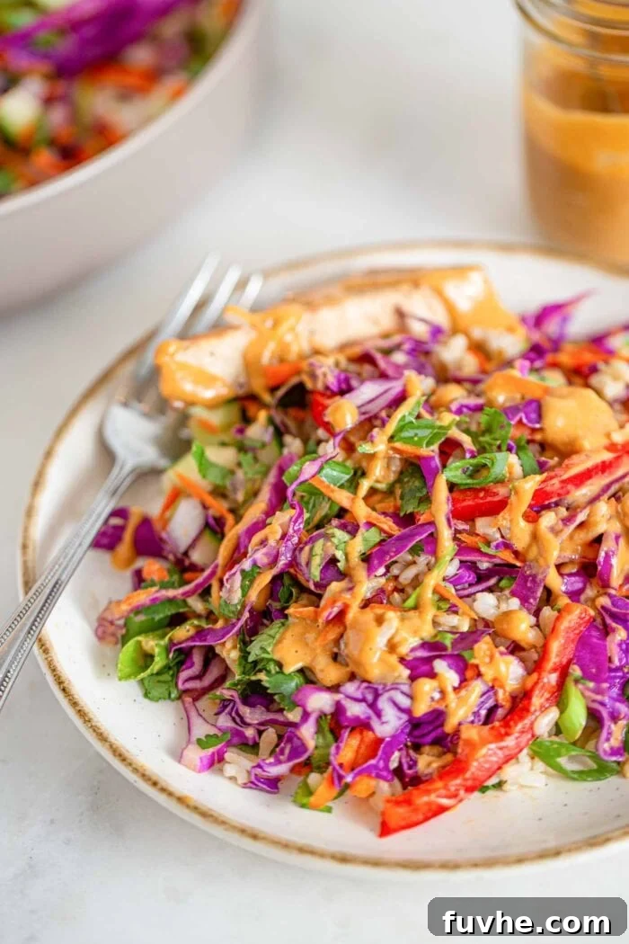 A vibrant plate of Thai chopped salad, richly adorned with crispy baked tofu, creamy peanut sauce, perfectly cooked brown rice, and a medley of fresh, colorful chopped vegetables.