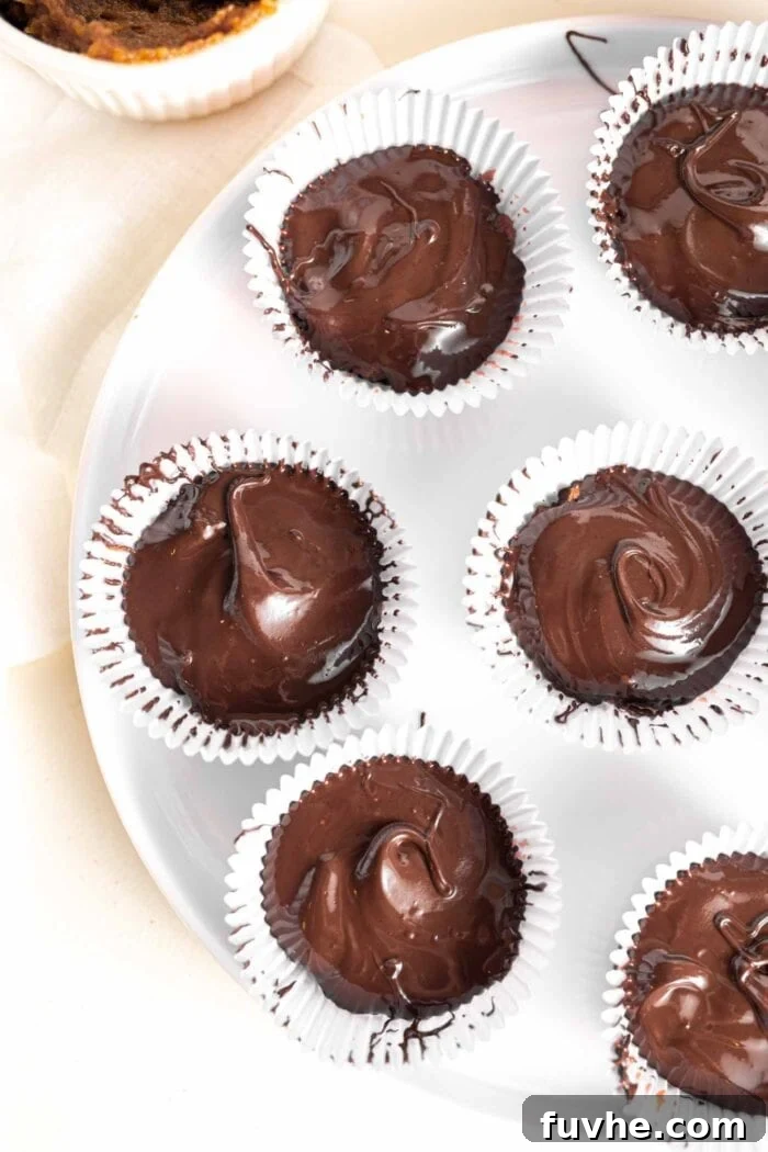 Melted chocolate being poured over date paste in muffin liners, forming the top layer of the chocolate cups.