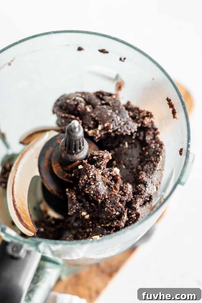 Fudgy No-Bake Brownie Bites 6 Raw brownie dough forming a thick, sticky mass in a food processor.