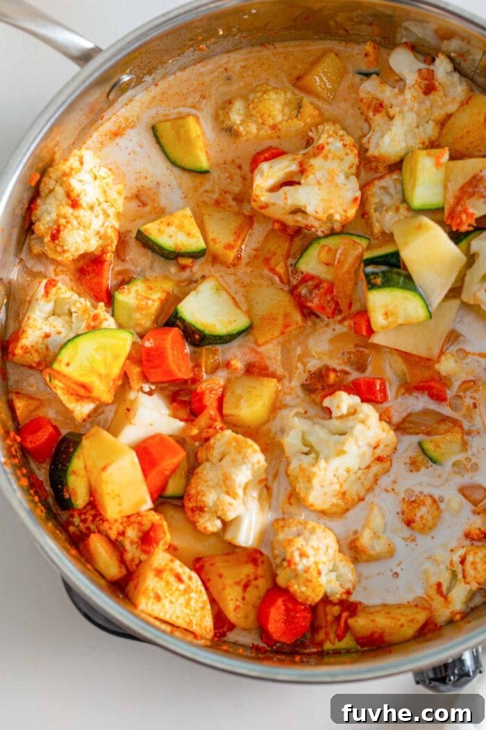 Golden Chickpea Potato Curry 5 Colorful vegetables like carrots, potatoes, cauliflower, and zucchini simmering perfectly in a creamy coconut milk and vegetable broth base in a large pot.