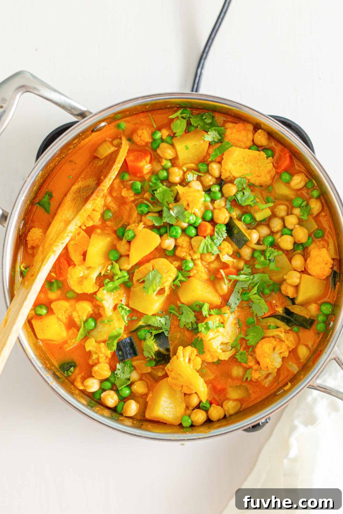Golden Chickpea Potato Curry 6 A large pot filled with a rich and vibrant chickpea and potato curry, complete with bright green peas, and a wooden spoon resting within the pot.