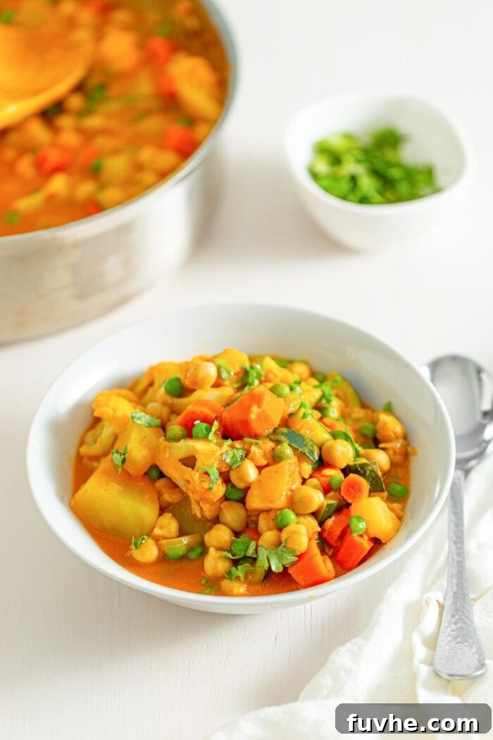 Golden Chickpea Potato Curry 7 A stunning bowl of vegan chickpea potato curry in the foreground, brimming with vegetables, chickpeas, and peas, with the simmering pot visible in the soft-focus background.