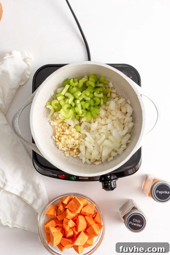 Onions, garlic, and celery gently cooking in a pot on a small induction stovetop, releasing their fragrant aromas.