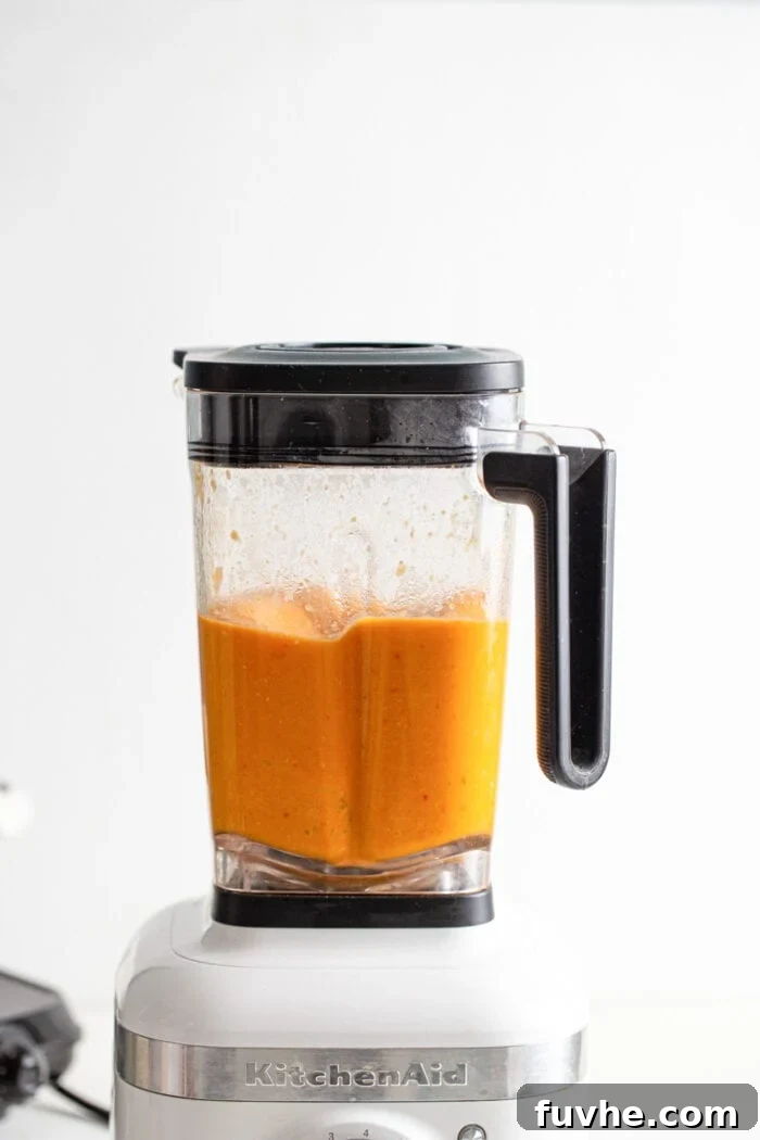 Creamy, blended sweet potato corn chowder swirling smoothly in a blender, ready to be combined with the remaining textured soup.