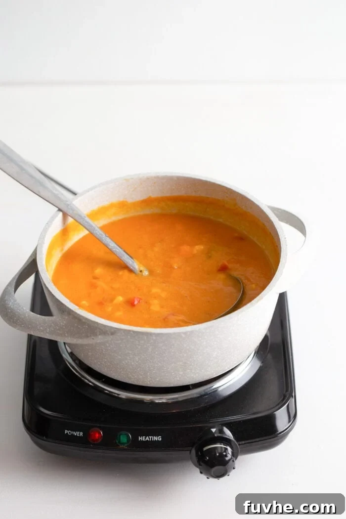 Creamy sweet potato corn chowder, perfectly blended and ready to serve, in a soup pot with a spoon resting in it.