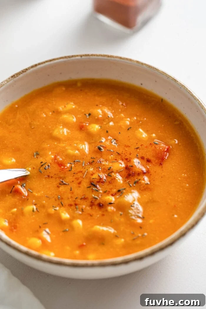 Close-up shot of a creamy sweet potato corn chowder in a rustic bowl, with a spoon resting invitingly, showcasing its rich texture and warm color.