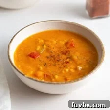Bowl of sweet potato corn chowder, garnished with fresh herbs. Another bowl of soup sits blurred in the background, suggesting a cozy meal setting.