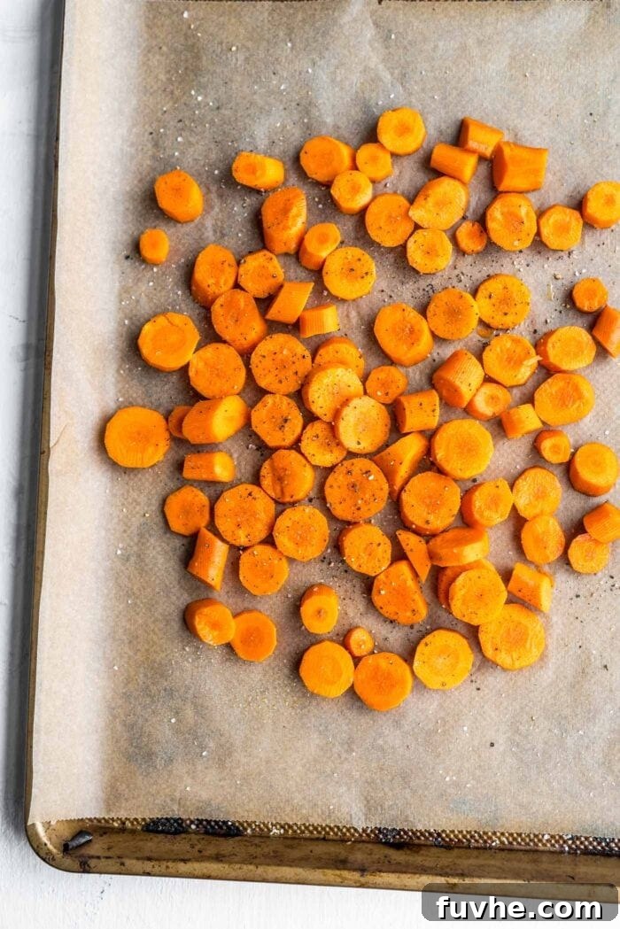 Chopped carrots, lightly seasoned with salt and pepper, arranged on a parchment paper-lined baking tray, ready for roasting to achieve their sweet, tender perfection.