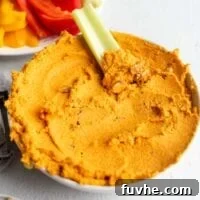 A bowl of roasted carrot hummus with a piece of celery dipped in it.