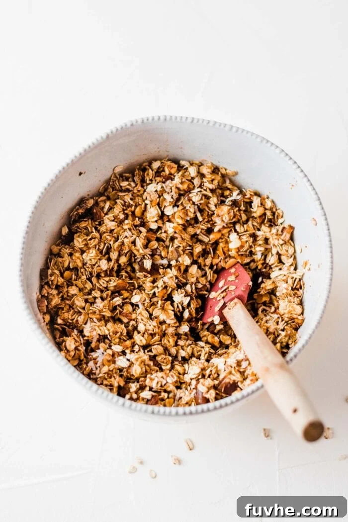 Cozy Pumpkin Crunch 4 Unbaked pumpkin spice latte granola mixture, rich with pumpkin and spices, being stirred in a mixing bowl with a spoon.