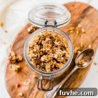 Open jar of homemade pumpkin spice latte granola sitting on a rustic cutting board with a spoon beside it, ready for breakfast.