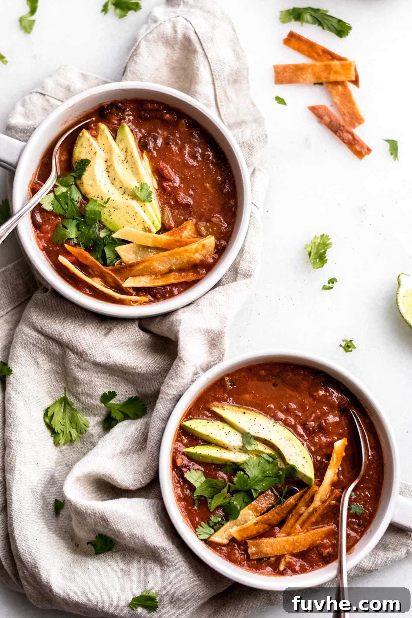 Two bowls of The Best Vegan Tortilla Soup, garnished with vibrant avocado slices, fresh cilantro, and crispy tortilla strips.