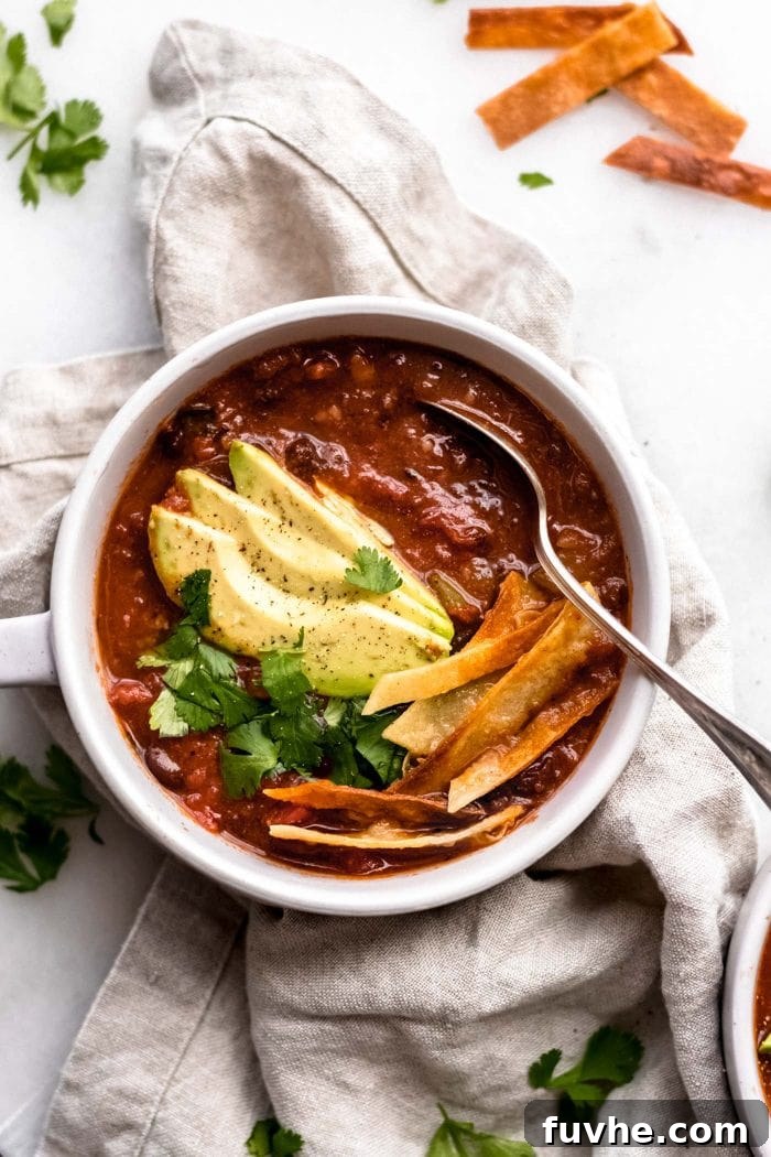 An inviting overhead shot of a bowl of vegan tortilla soup, garnished perfectly with slices of avocado, vibrant cilantro, and an abundance of golden, crispy tortilla strips.