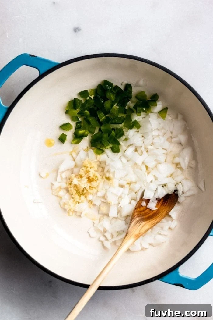 Diced onions, minced garlic, and sliced jalapeno sizzling in olive oil within a soup pot, forming the aromatic base for vegan tortilla soup.