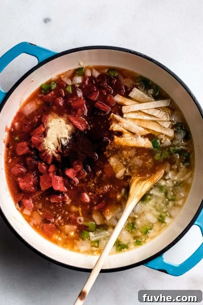 A colorful array of ingredients including garlic powder, diced tomatoes, minced garlic, diced onion, vegetable broth, and sliced jalapeño mingling in a soup pot.