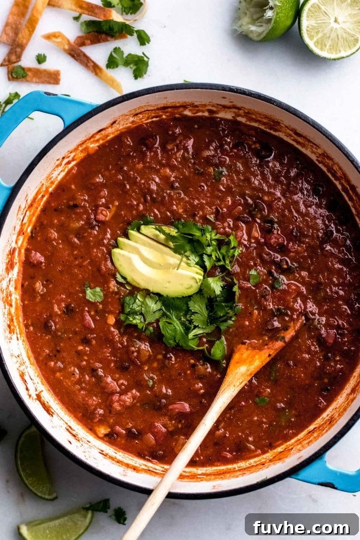 The best vegan tortilla soup, now finished and ready to serve, glistening in a soup pot and topped generously with fresh cilantro and creamy avocado slices.