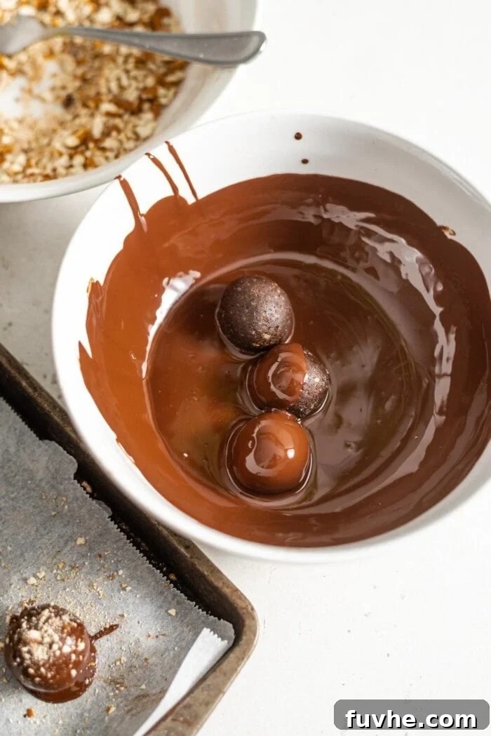 Salty Sweet Vegan Chocolate Truffles 6 Three chocolate truffles submerged in a bowl of glistening melted chocolate, ready for coating.