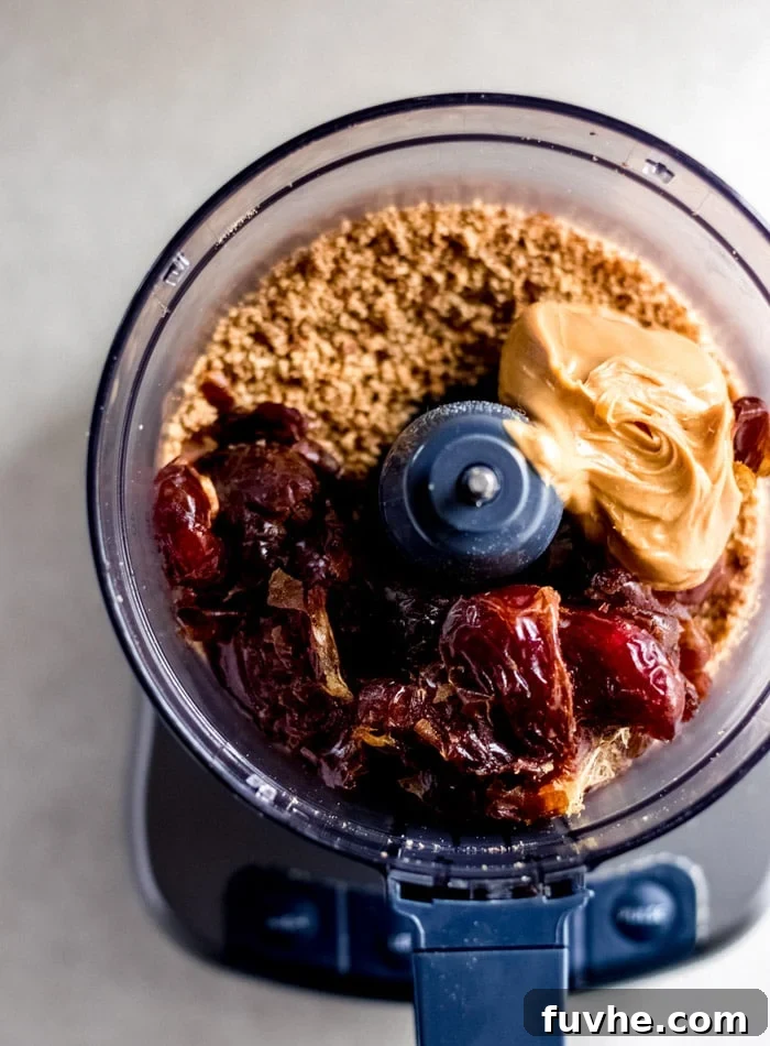 Close-up of dates, creamy peanut butter, and finely crushed almonds ready to be blended in a food processor, highlighting the simple, wholesome ingredients.