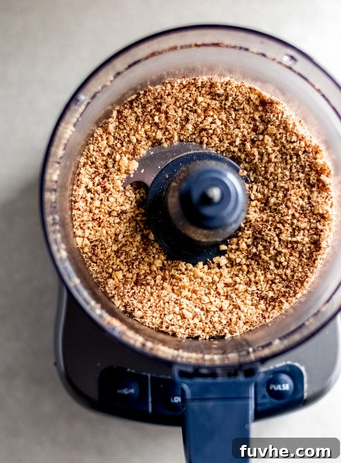 Raw almonds finely blended into a grainy flour texture within a food processor bowl, ready for the next ingredients.