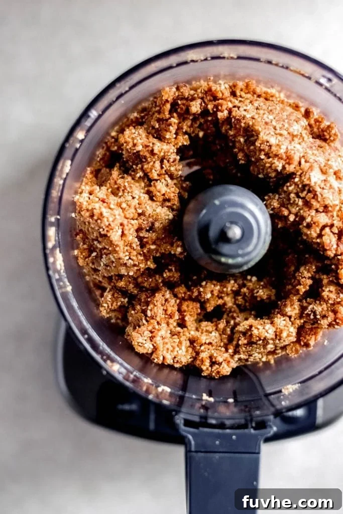 The food processor bowl contains a thick, sticky dough, a blend of dates, peanut butter, and almonds, forming the base for energy bars.