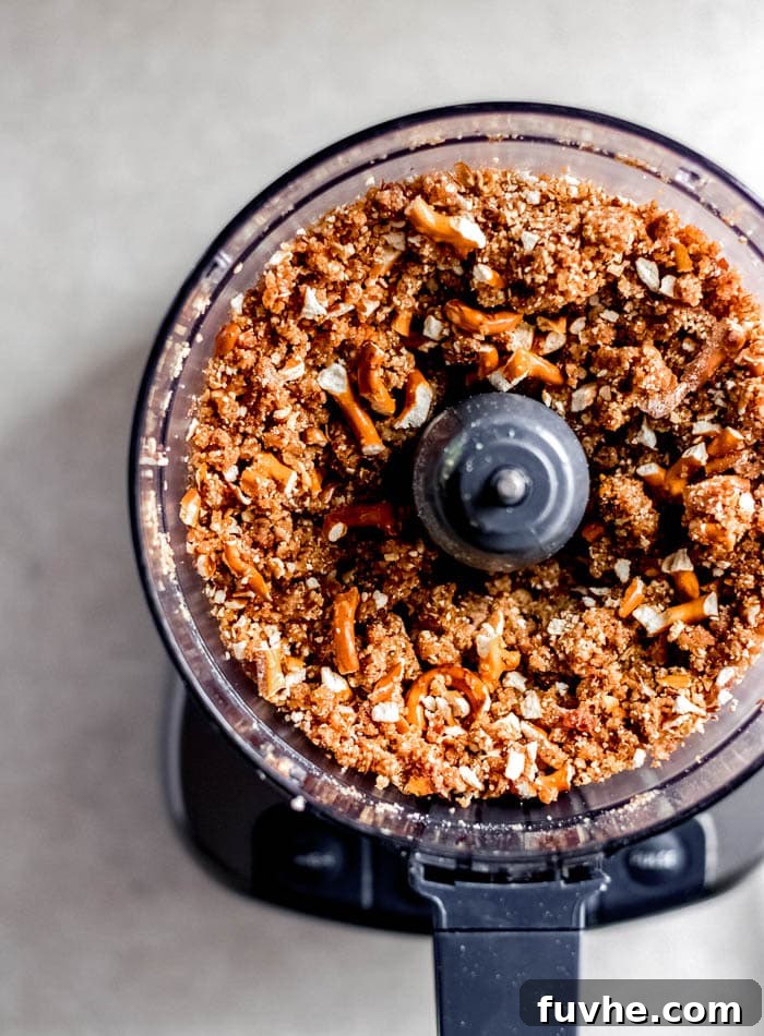 The raw energy bar dough with visible pretzel pieces mixed in, ready for pressing, showcased within the food processor.