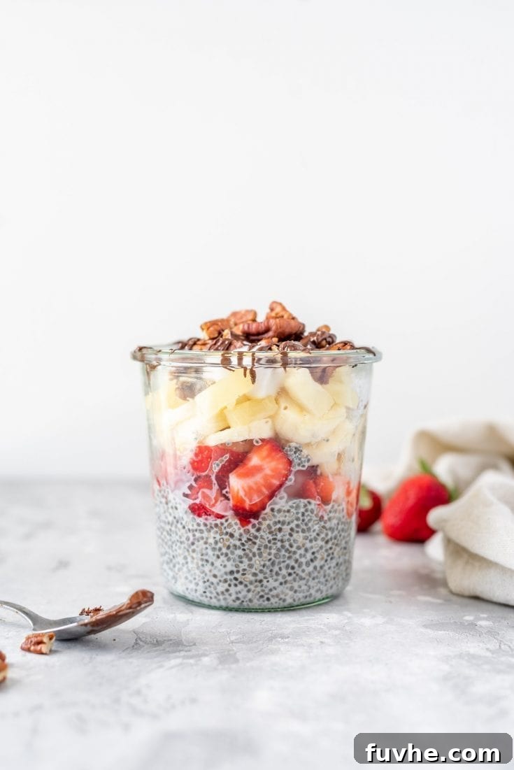A vibrant banana split chia seed pudding parfait layered with chocolate chia pudding, banana, strawberries, and whipped cream in a tall glass.