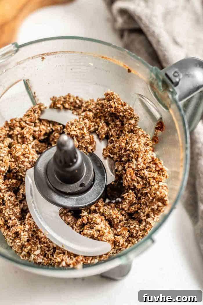 Close-up of blended raw energy ball dough in a food processor, showing its thick, sticky texture.