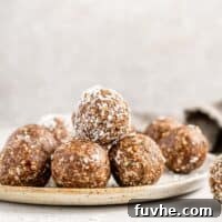 A stack of raw energy balls on a plate, garnished with shredded coconut.
