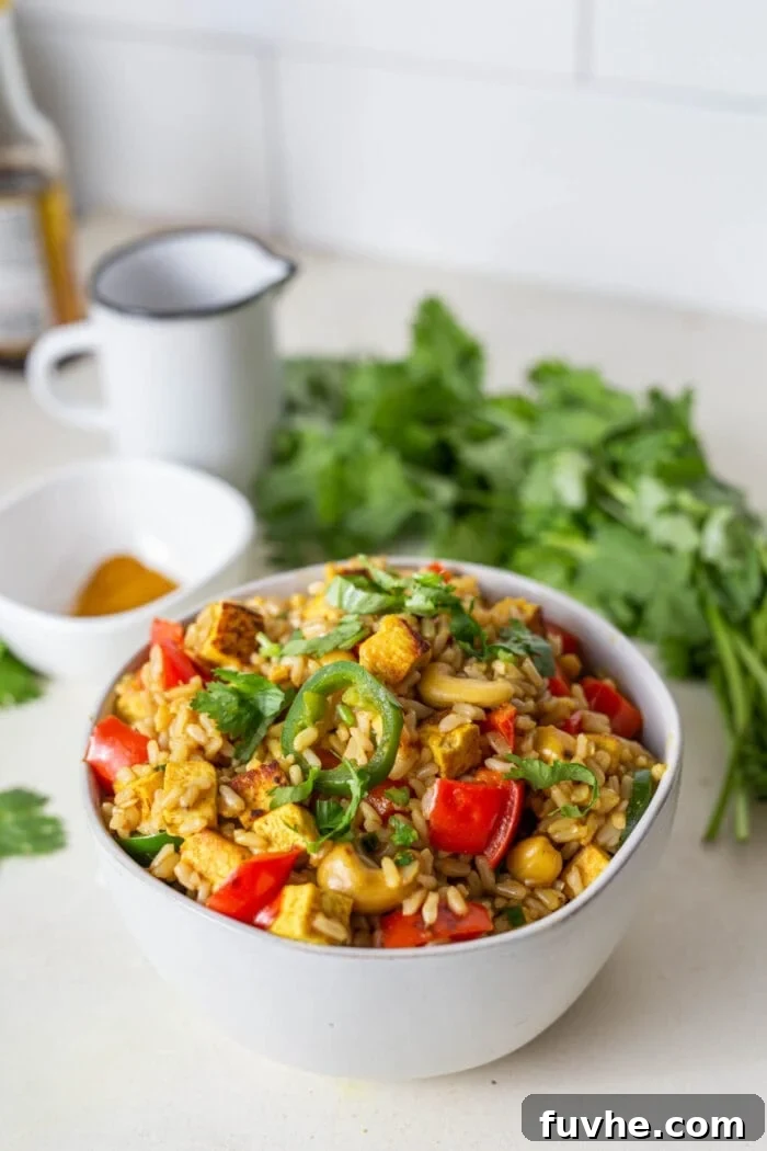 Crispy Cashew Tofu Fried Rice 7 A close-up shot of a bowl of Cashew Tofu Fried Rice, perfectly garnished with fresh cilantro, and a fork resting within, ready for a delicious bite.