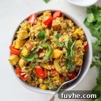 A vibrant bowl of Cashew Tofu Fried Rice with green onions and cilantro garnish, ready to be enjoyed with a fork.