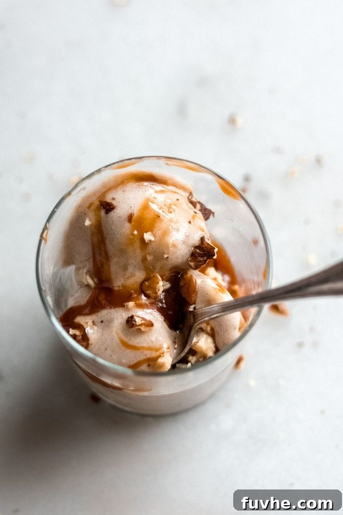 Glass filled with vegan banana ice cream topped with nuts and caramel sauce.
