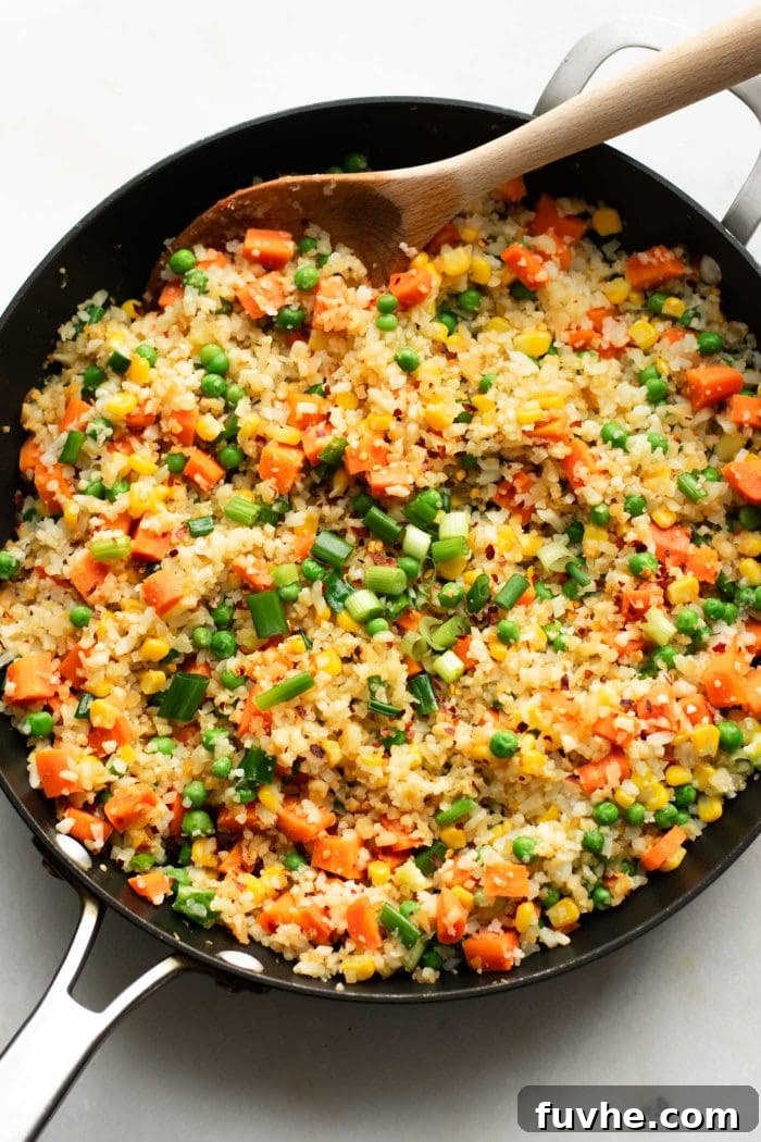 Plant-Based Cauliflower Fried Rice 7 All ingredients brilliantly combined and stir-fried in a hot pan, showcasing perfectly cooked cauliflower fried rice, featuring tender carrots, vibrant peas, sweet corn, and fresh green onion, ready to be served and enjoyed.