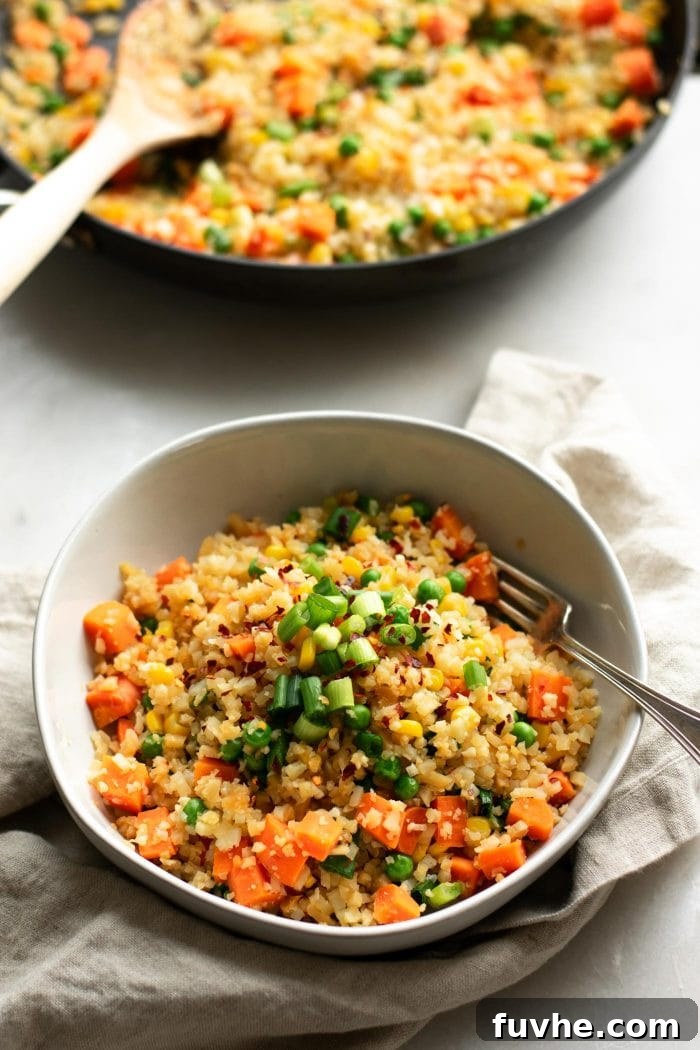 Plant-Based Cauliflower Fried Rice 8 A close-up shot of a healthy bowl of vegan cauliflower fried rice, beautifully topped with fresh green onions. A fork is delicately poised in the dish, ready to scoop up the vibrant mix of tender carrots, sweet peas, and golden corn kernels.