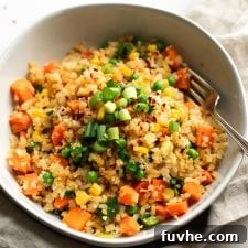 A bowl of fried cauliflower rice with carrots, peas and corn, topped with green onion with a fork in the bowl.